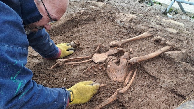 An archaeologist brushes dust from a skeleton in an archaeological dig